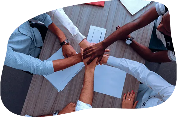 5 pessoas sentdas em uma mesa, com as maos se tocando no centro da mesa